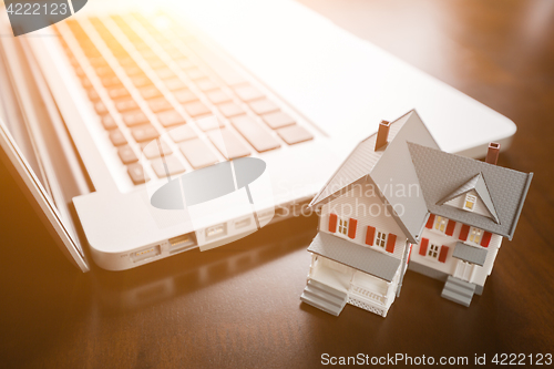 Image of Miniature House And Laptop Computer Resting on Desktop.