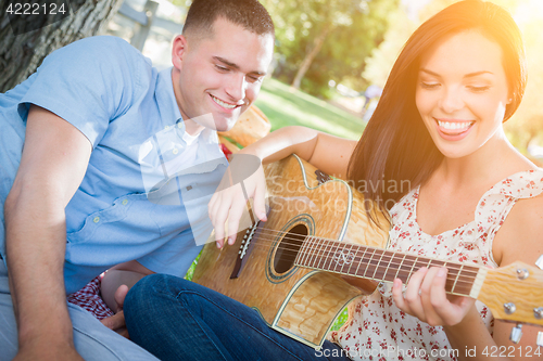 Image of Happy Mixed Race Couple at the Park Playing Guitar and Singing S