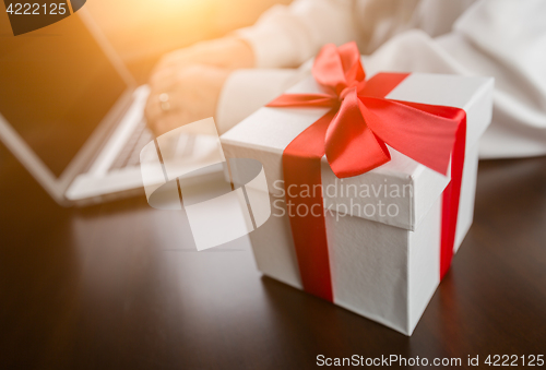 Image of White Gift Box with Red Ribbon and Bow Near Man Typing on Laptop