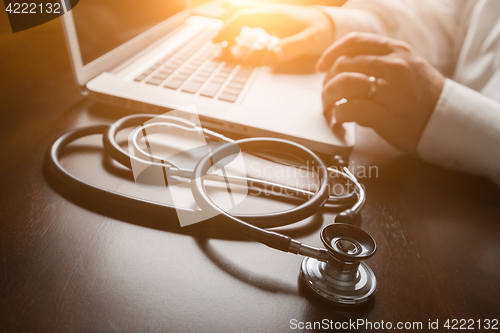Image of Medical Stethoscope Resting on Desk As Male Hands Type on Comput