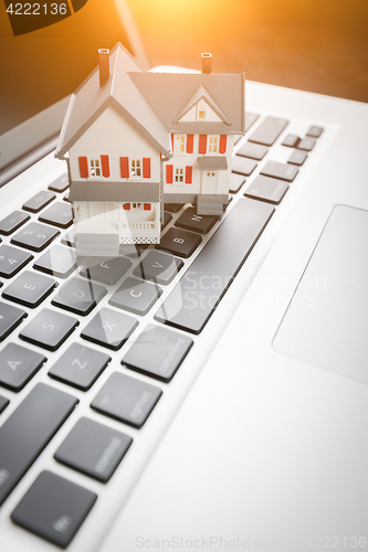 Image of Miniature House And Laptop Computer Resting on Desktop.