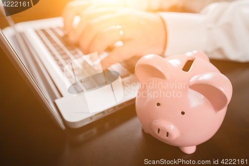 Image of Piggy Bank Near Male Hands Typing on Laptop Computer.