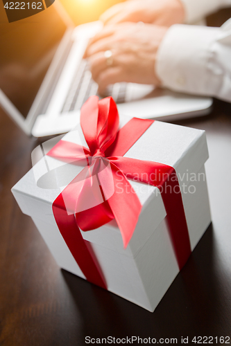 Image of White Gift Box with Red Ribbon and Bow Near Man Typing on Laptop