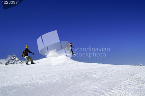 Image of Two snowboarders jump in snow park at ski resort on sunny winter