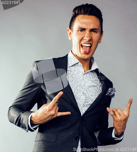 Image of young pretty business man standing on grey background, modern hairstyle, gesturing emotional