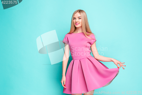 Image of Smiling beautiful young woman in pink mini dress posing at studio