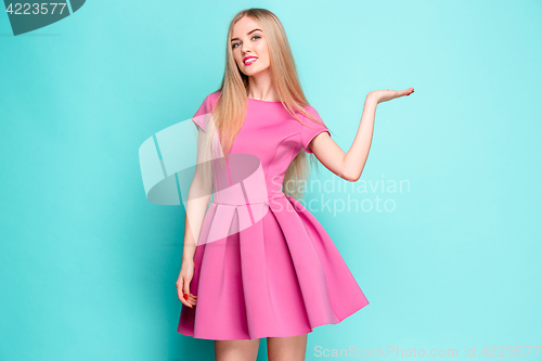 Image of Smiling beautiful young woman in pink mini dress posing, presenting something