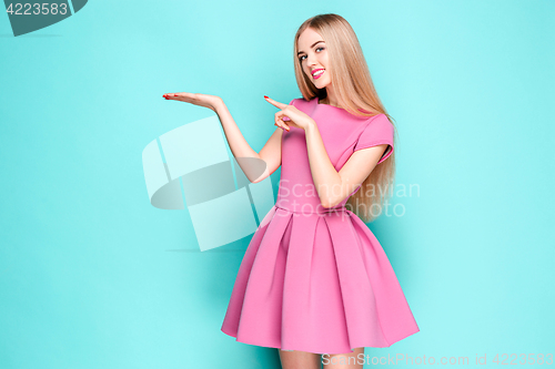 Image of Smiling beautiful young woman in pink mini dress posing, presenting something