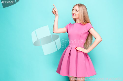 Image of Smiling beautiful young woman in pink mini dress posing, presenting something