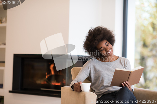 Image of black woman reading book  in front of fireplace