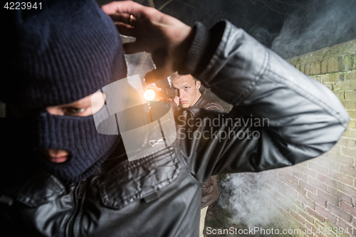 Image of Policeman aiming pistol towards busted masked gangster at night