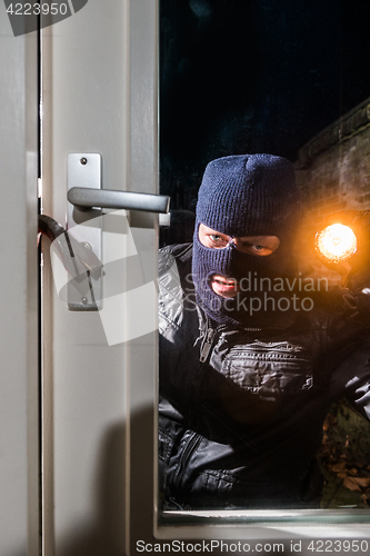 Image of Masked intruder holding torch while trying to open window with c