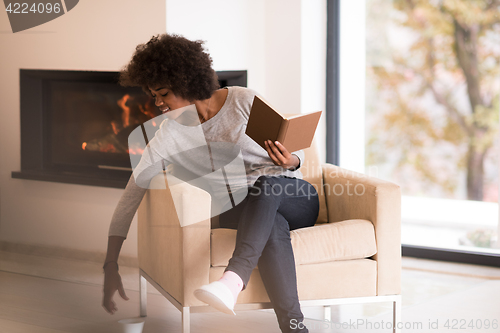 Image of black woman reading book  in front of fireplace