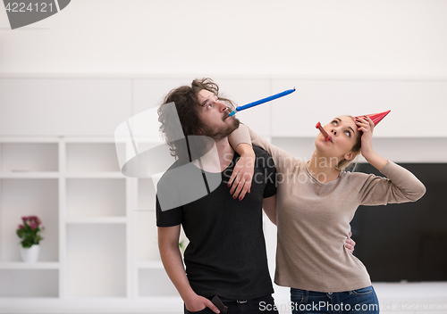 Image of couple in party hats blowing in whistle