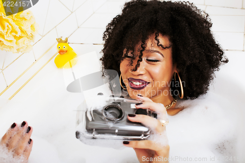 Image of young afro-american teen girl laying in bath with foam, wearing 