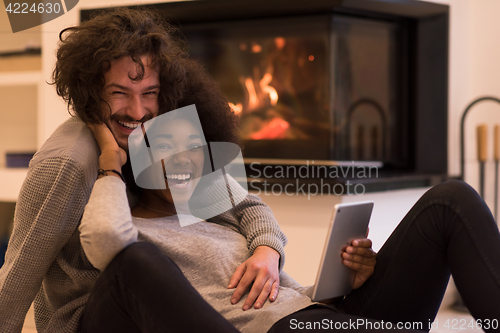 Image of multiethnic couple using tablet computer on the floor