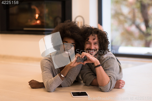 Image of multiethnic couple showing a heart with their hands on the floor