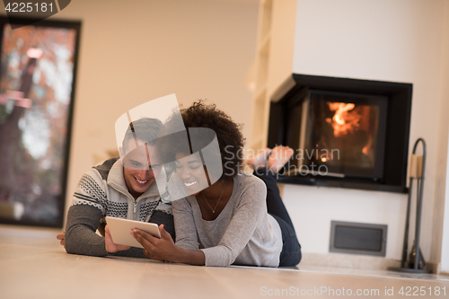 Image of multiethnic couple using tablet computer on the floor
