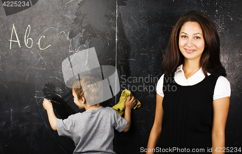 Image of little cute boy with young teacher in classroom studying at blac