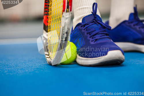 Image of Legs of young girl in a closed tennis court with ball and racket