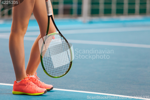 Image of Legs of young girl in a closed tennis court with racket