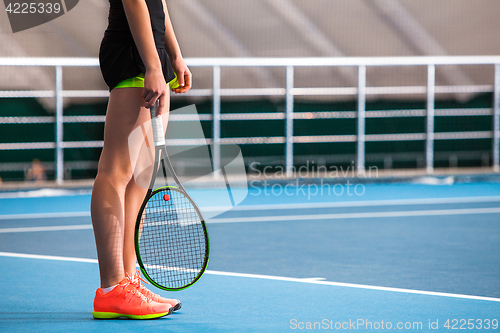 Image of Legs of young girl in a closed tennis court with ball and racket