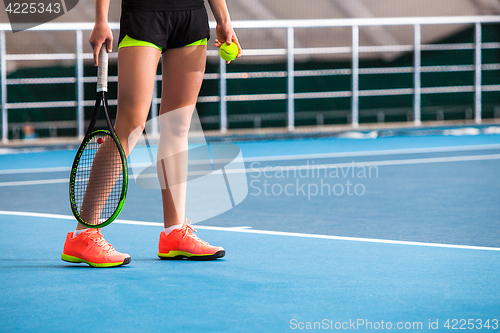 Image of Legs of young girl in a closed tennis court with ball and racket