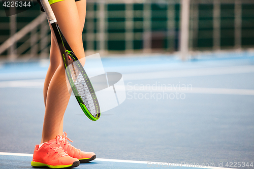 Image of Legs of young girl in a closed tennis court with racket