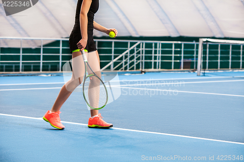 Image of Legs of young girl in a closed tennis court with ball and racket