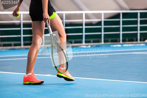 Image of Legs of young girl in a closed tennis court with ball and racket