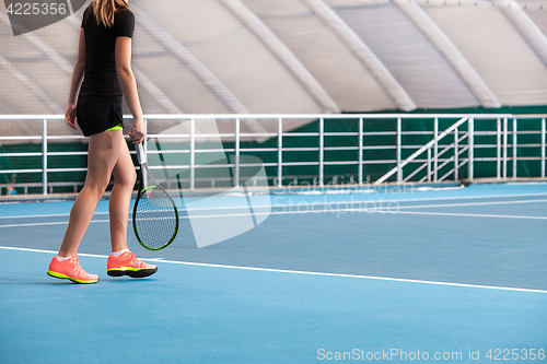 Image of Legs of young girl in a closed tennis court with ball and racket