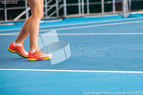 Image of Legs of young girl in a closed tennis court with ball and racket