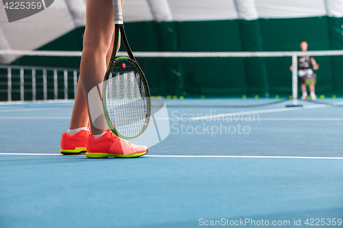 Image of Legs of young girl in a closed tennis court with ball and racket
