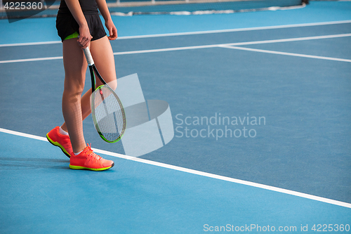 Image of Legs of young girl in a closed tennis court with ball and racket