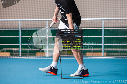Image of Legs of man in a closed tennis court with ball and racket