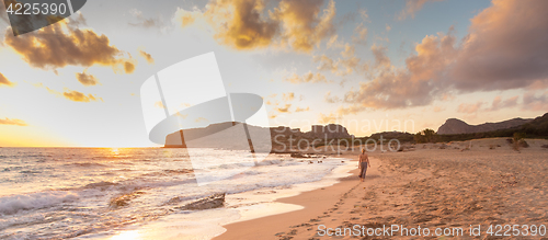 Image of Woman walking on sandy beach at sunset.