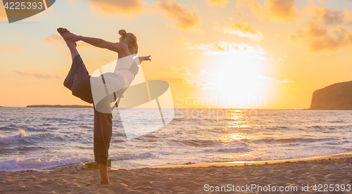 Image of Woman practicing yoga on sea beach at sunset.