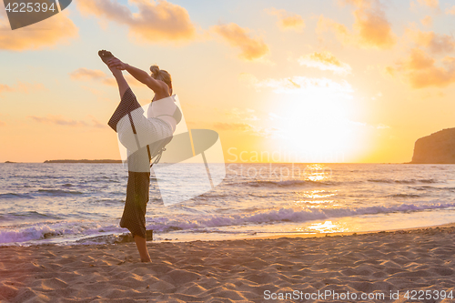 Image of Woman practicing yoga on sea beach at sunset.