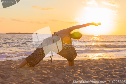 Image of Woman practicing yoga on sea beach at sunset.