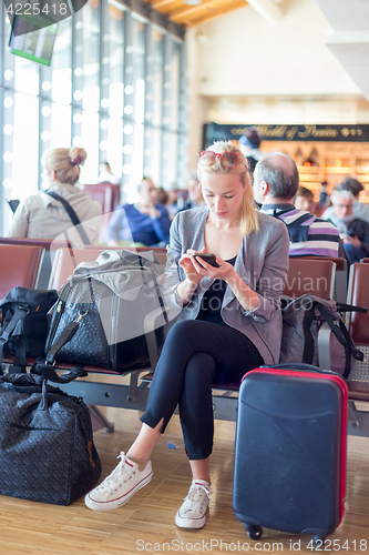 Image of Female traveler using cell phone while waiting on airport.