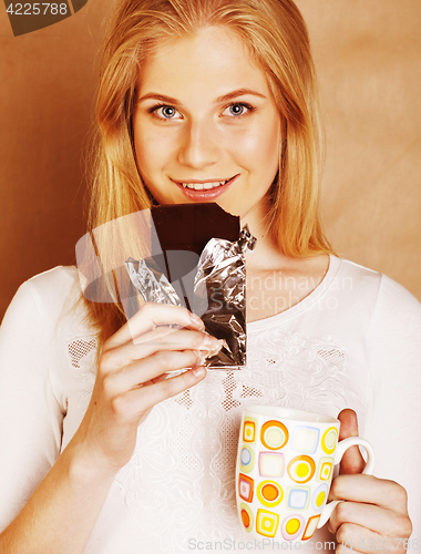 Image of young cute blond girl eating chocolate and drinking coffee close