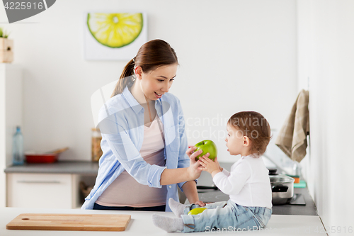 Image of mother giving green apple to baby at home kitchen