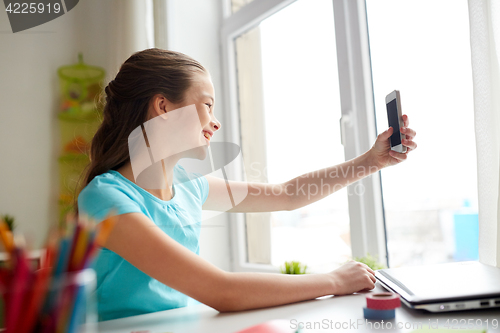 Image of happy girl with smartphone taking selfie at home