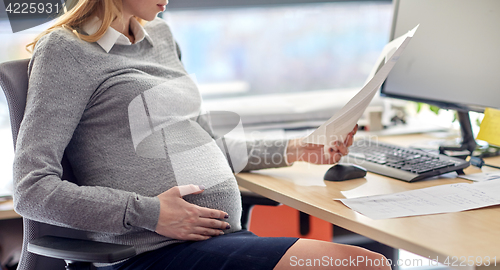 Image of pregnant businesswoman reading papers at office