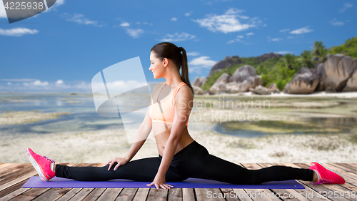 Image of smiling woman doing splits on mat over beach