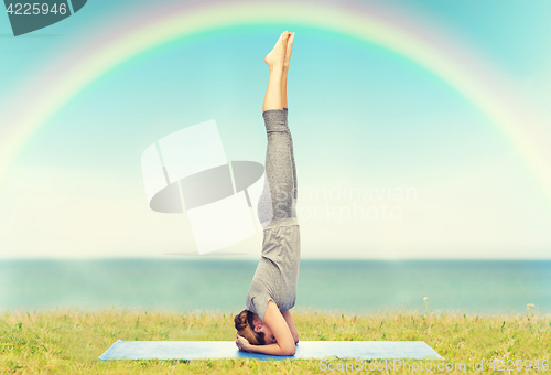 Image of woman making yoga in headstand pose on mat