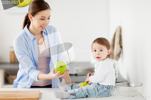 Image of mother giving green apple to baby at home kitchen