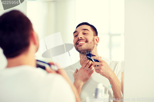 Image of man shaving beard with trimmer at bathroom