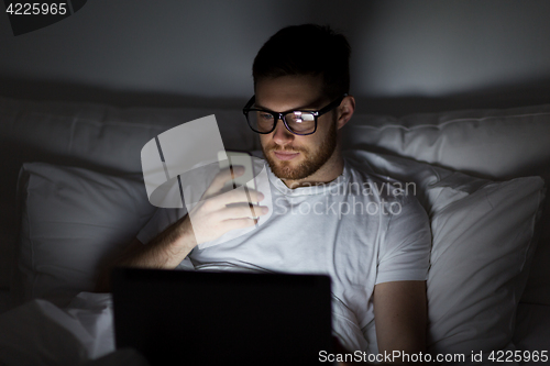 Image of man with laptop and smartphone at night in bed