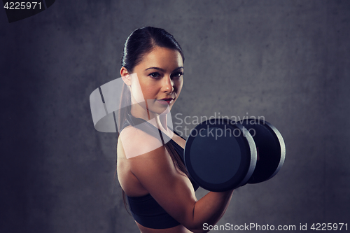 Image of young woman flexing muscles with dumbbells in gym